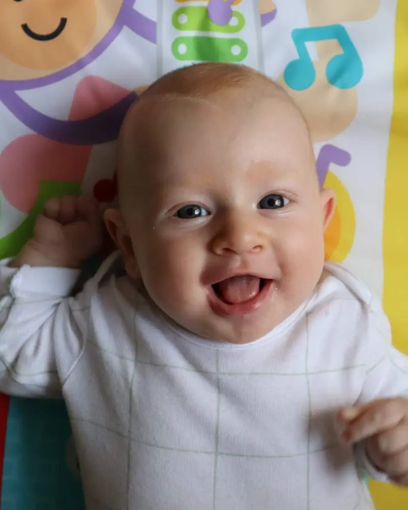 Un bebé sonríe con la boca abierta, tumbado en su manta de juegos.