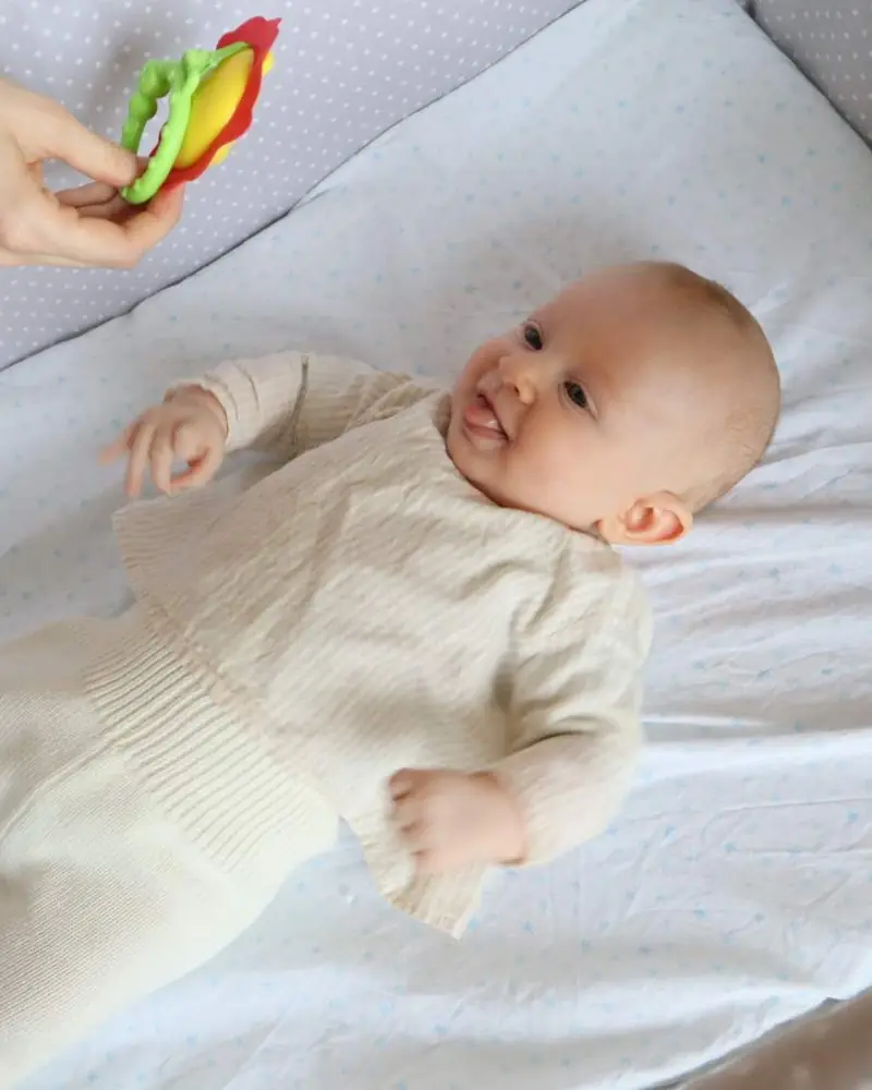 Un bebé tumbado en la cuna mira el sonajero que le acercan.